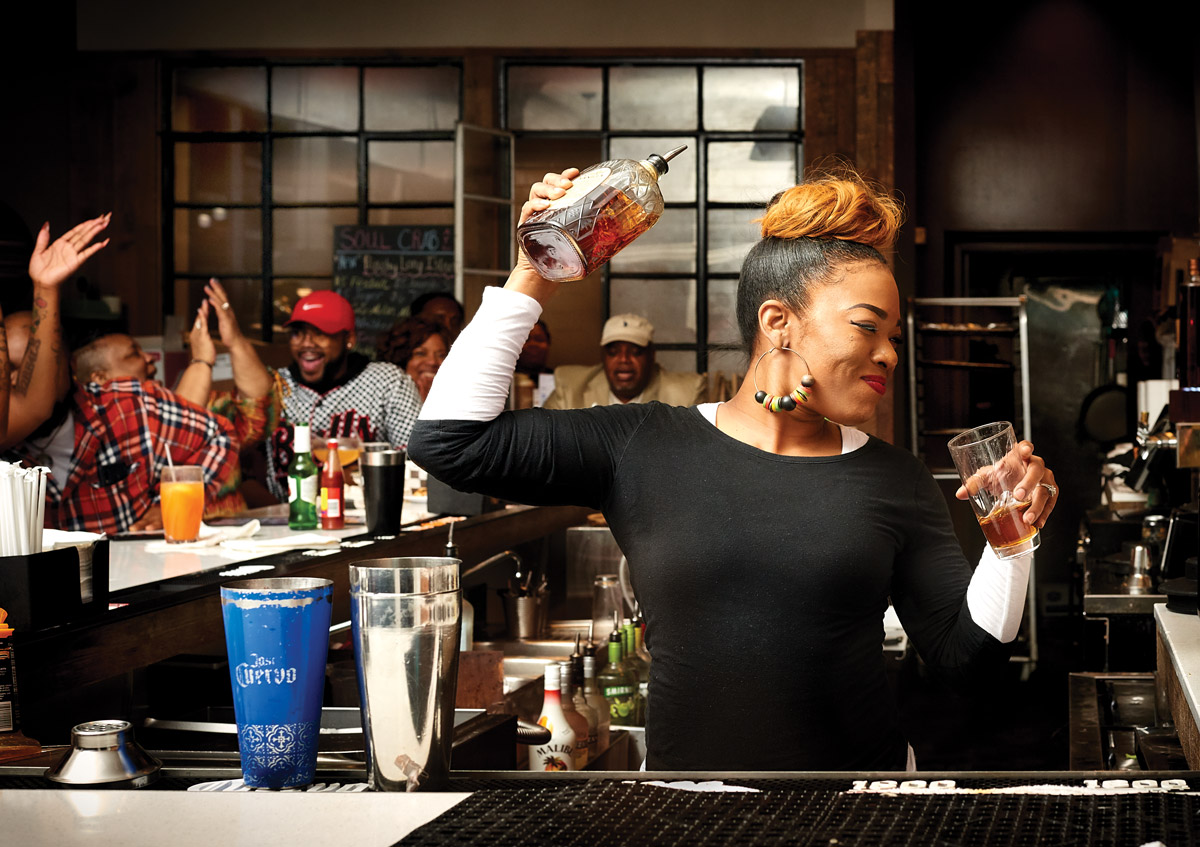 A Soul Crab bartender smiles while making a cocktail and people are laughing around the bar