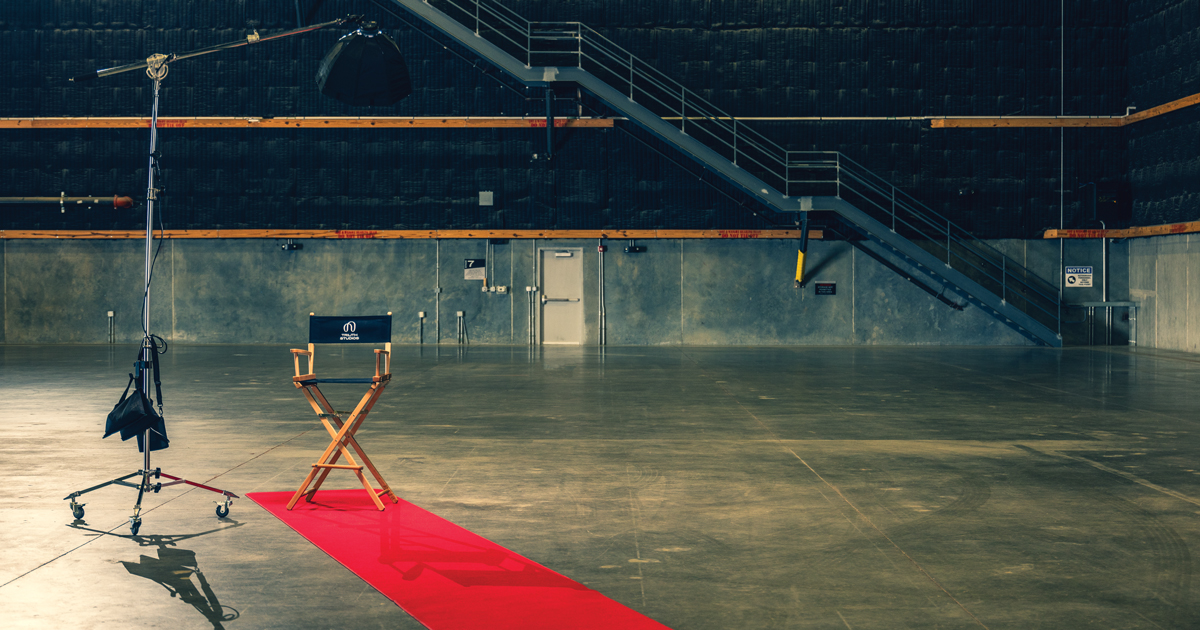A directors chair at the end of a red carpet in an empty sound stage