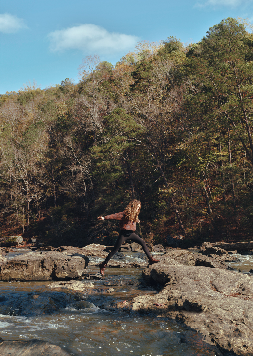 A woman hopping across rocks in a river at Sweetwater Creek State Park