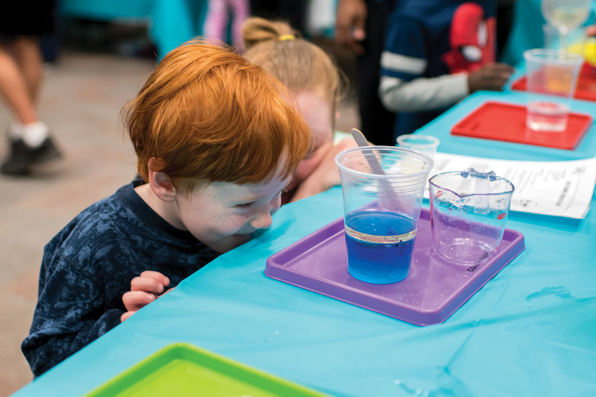 Two kids laughing while looking at a cup of colorful liquid