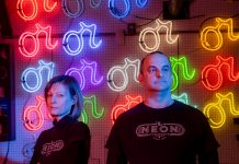 Vyvyan Hughes and Craig Weido in front of a wall of neon signs