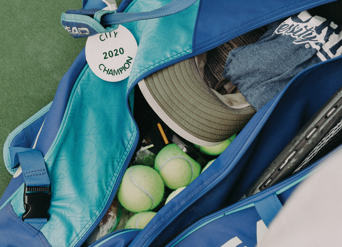 A bag filled with tennis equipment and clothes that has an ALTA bag tag