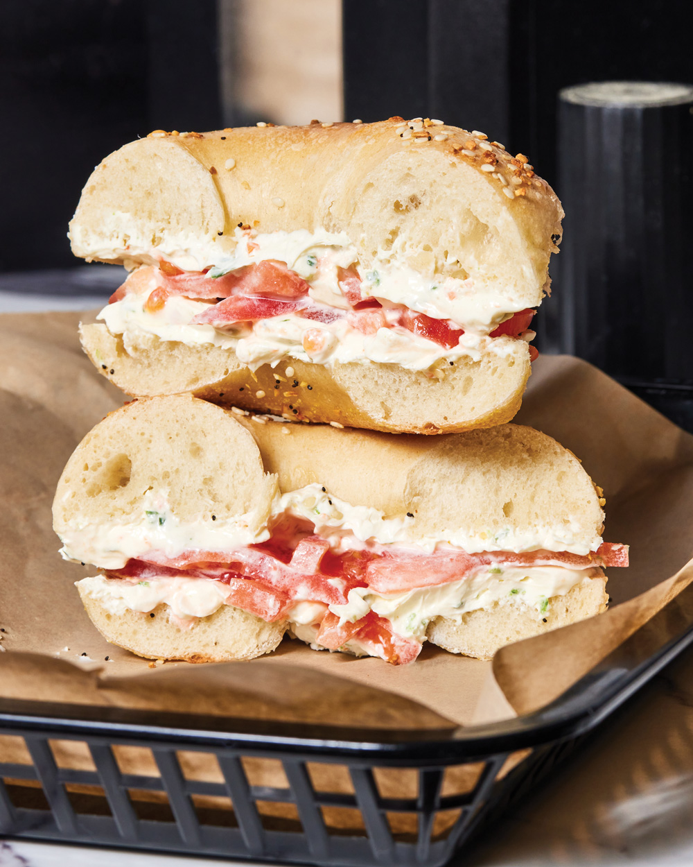 Two halves of an everything bagel stacked on top of each other with veggie cream cheese and tomato