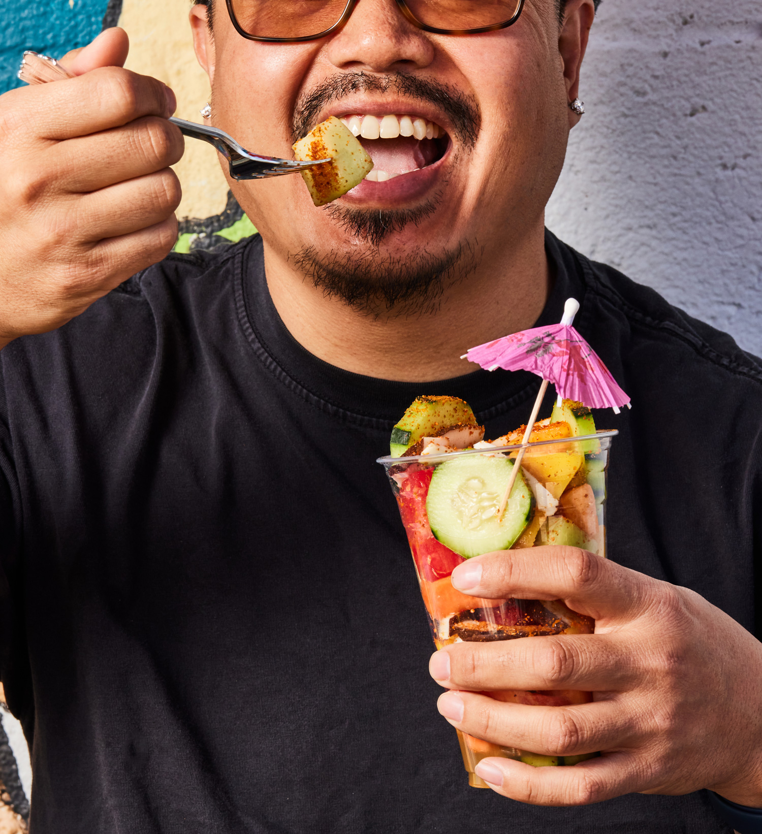 A man eating a fruit cup with a small pink umbrella coming out on top as decoration