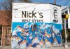The outside of Nick's Food To Go building, with blue graffiti words and a graffiti women with the words "Stay classy" above her
