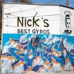 The outside of Nick's Food To Go building, with blue graffiti words and a graffiti women with the words "Stay classy" above her