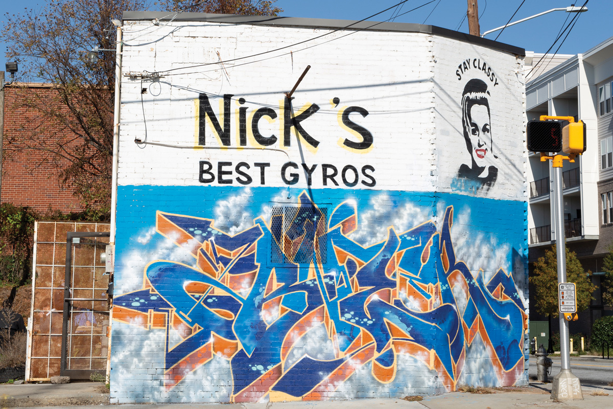 The outside of Nick's Food To Go building, with blue graffiti words and a graffiti women with the words