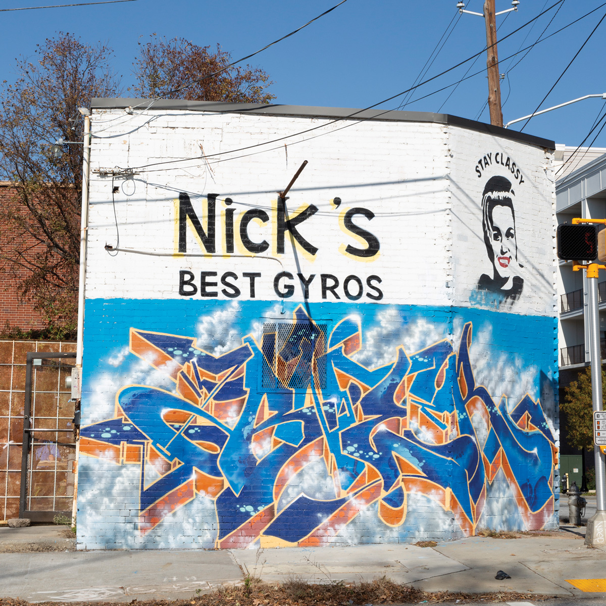 The outside of Nick's Food To Go building, with blue graffiti words and a graffiti women with the words "Stay classy" above her
