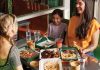Friends laughing while sitting at a table with multiple trays of food and drinks