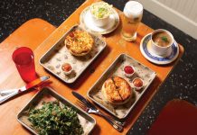 New Zealand meat pies, beer, and side dishes sit a top a wooden dining table