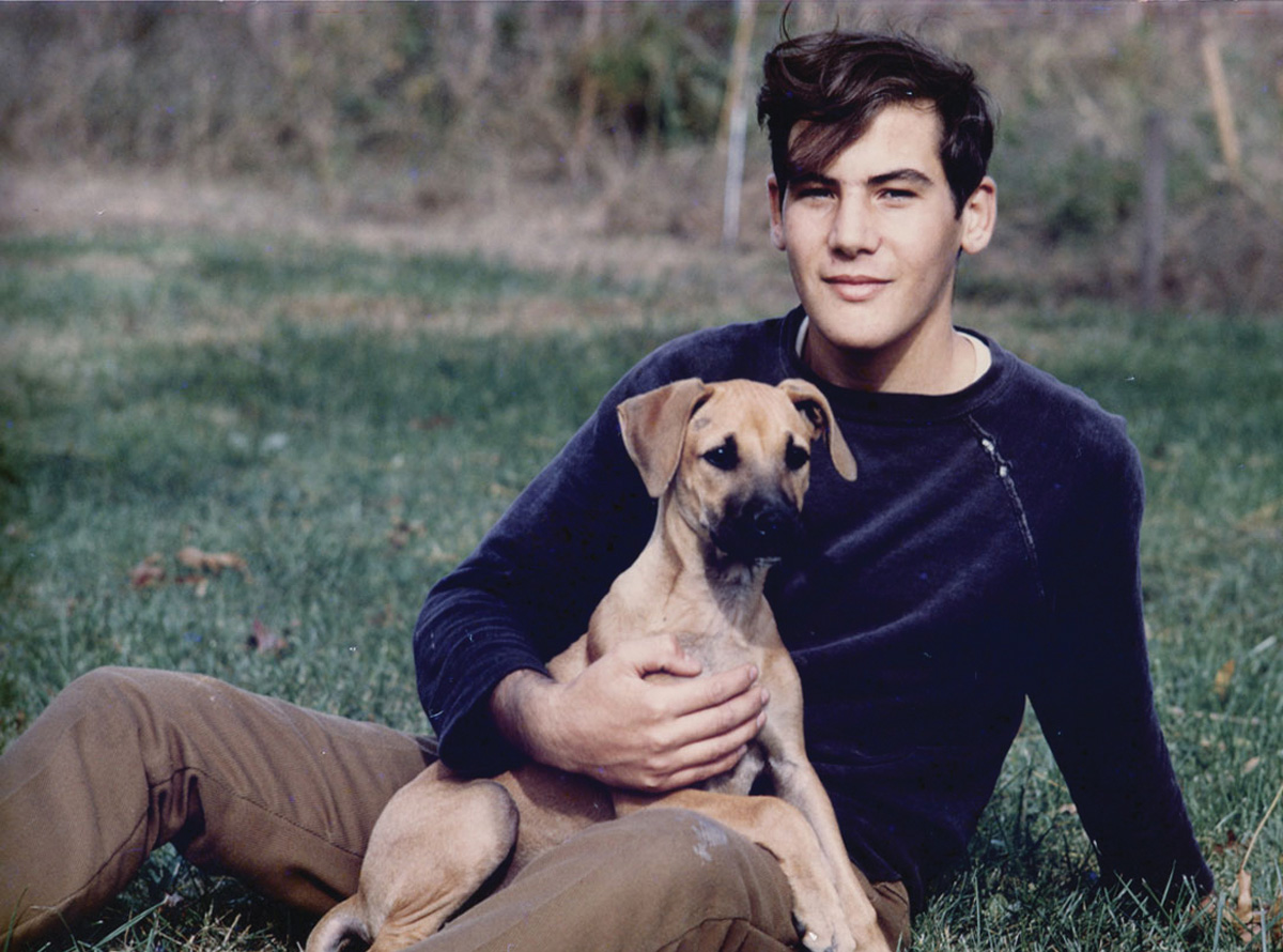 a younger Michael Quattroch sits on the grass while hoding a dog