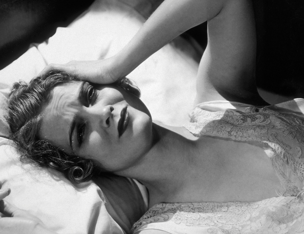 a woman lays in bed with her hand on her head