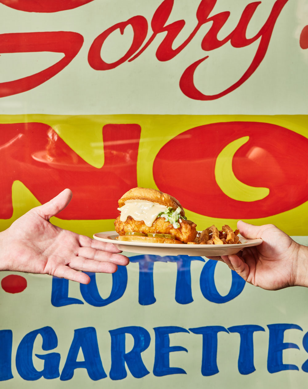 A person handing a grilled fish sandwich on a plate to someone else
