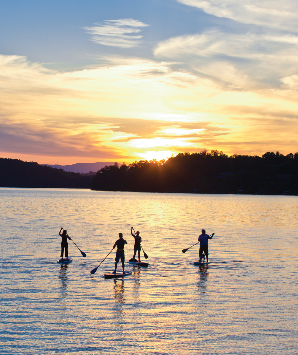 four people paddleboarding along a lake at sunset