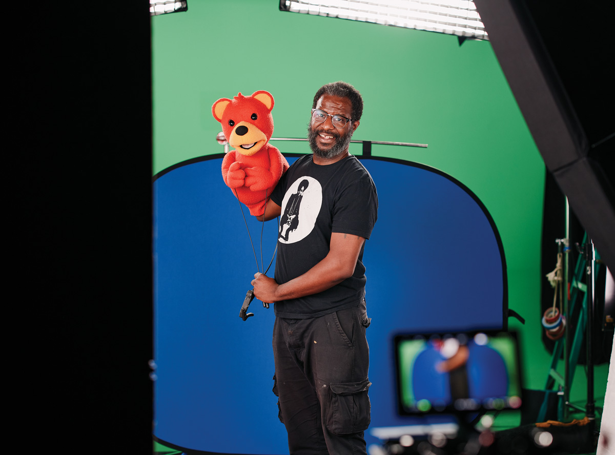 Raymond Carr holds a puppet in front of a camera