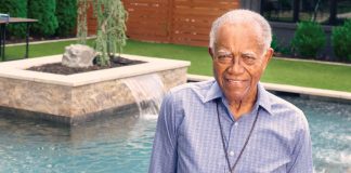 J.T. Johnson smiles in a yard with manicured greenery and a pool behind him