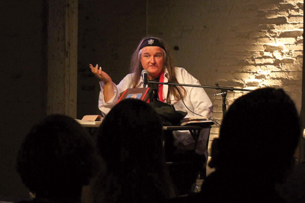 a speaker stands in a dark room, addressing the silhouetted audience
