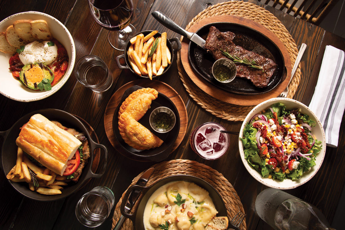 a spread of authentic argentine food including steak, empanadas, fries, and wine