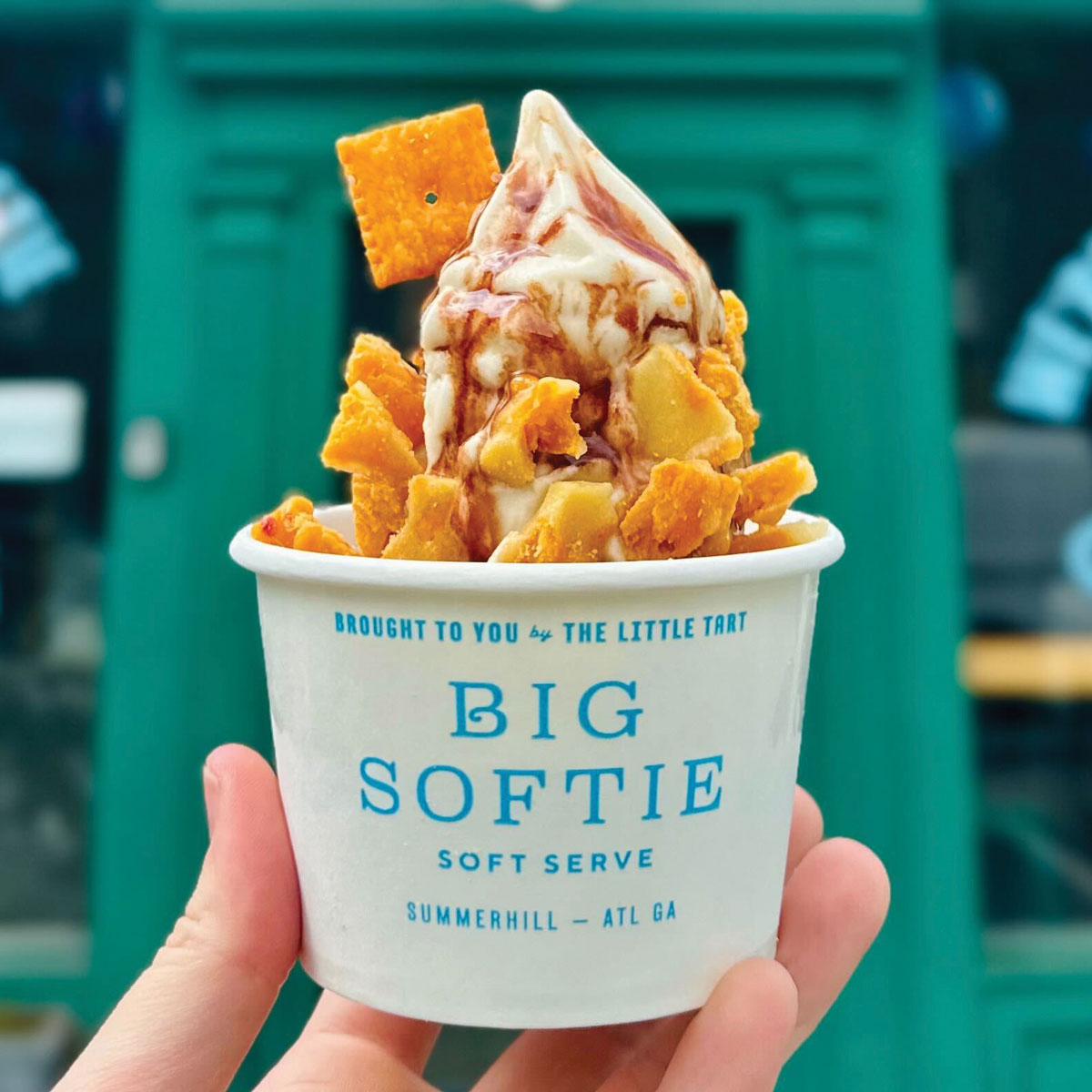 A person holding a Soft-Serve with Cheez-It Brittle in front of Big Softie's green door
