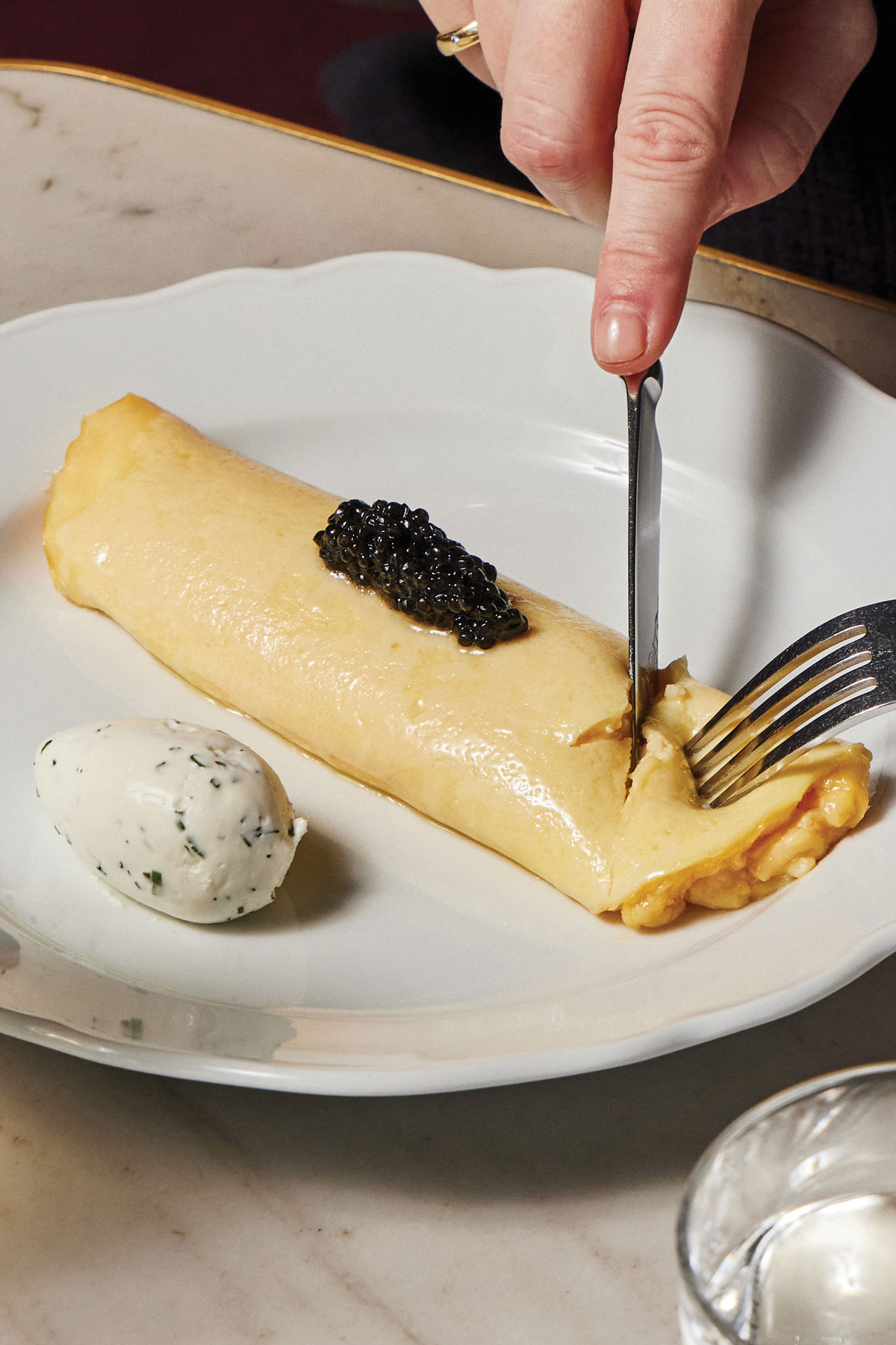 A fork and knife cut into an omelette with caviar and creme friache