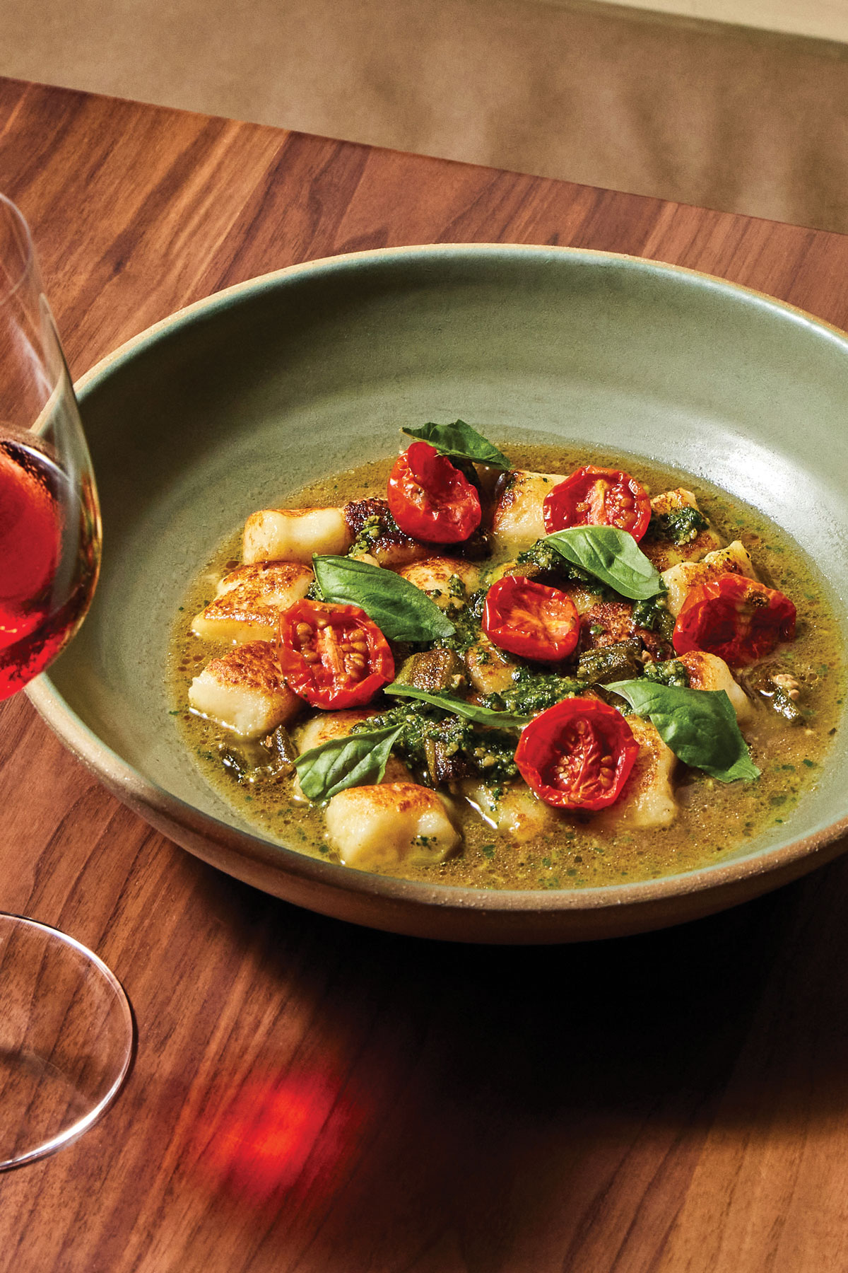 Gnocchi in a bowl next to a glass of red wine