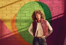 a model smiles in front of a pink, yellow, orange, and green mural