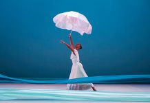 a dancer holds a white umbrella in with a blue backdrop behind her and two different shades of blue fabric in front of her