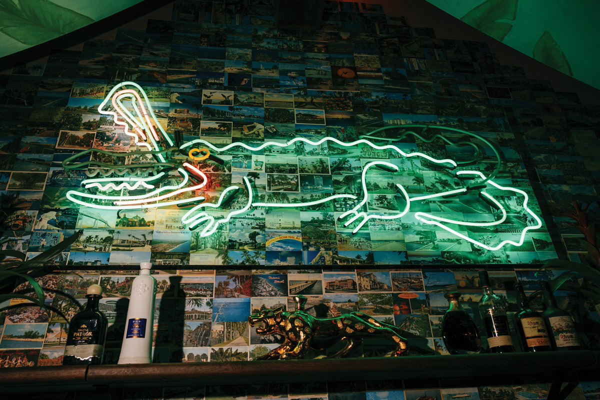 a neon sign of a crocodile sits atop a wall covered in postcards