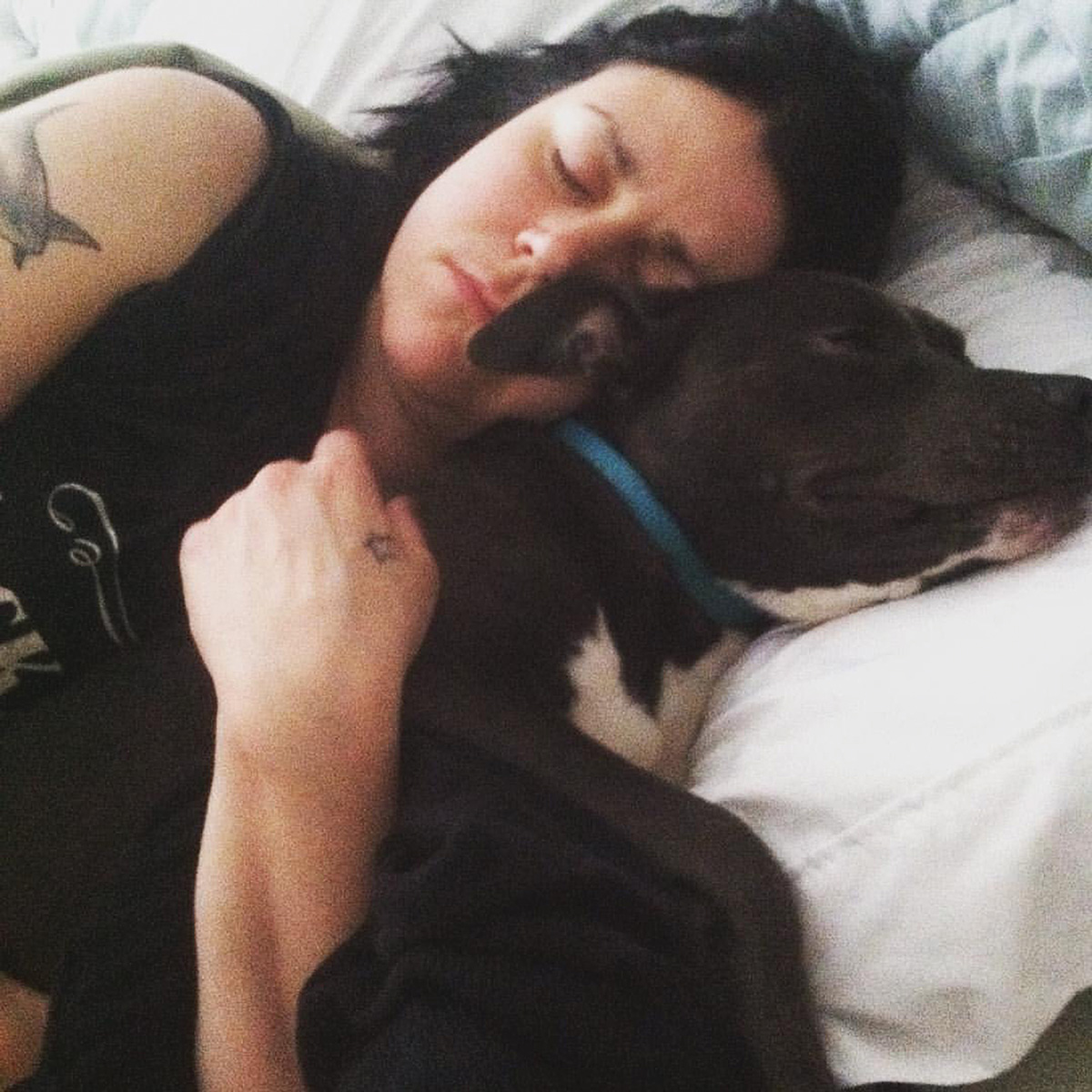 Katie Janness has her eyes closed as she lays in bed, hugging her dog, Bowie