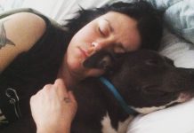 Katie Janness has her eyes closed as she lays in bed, hugging her dog, Bowie