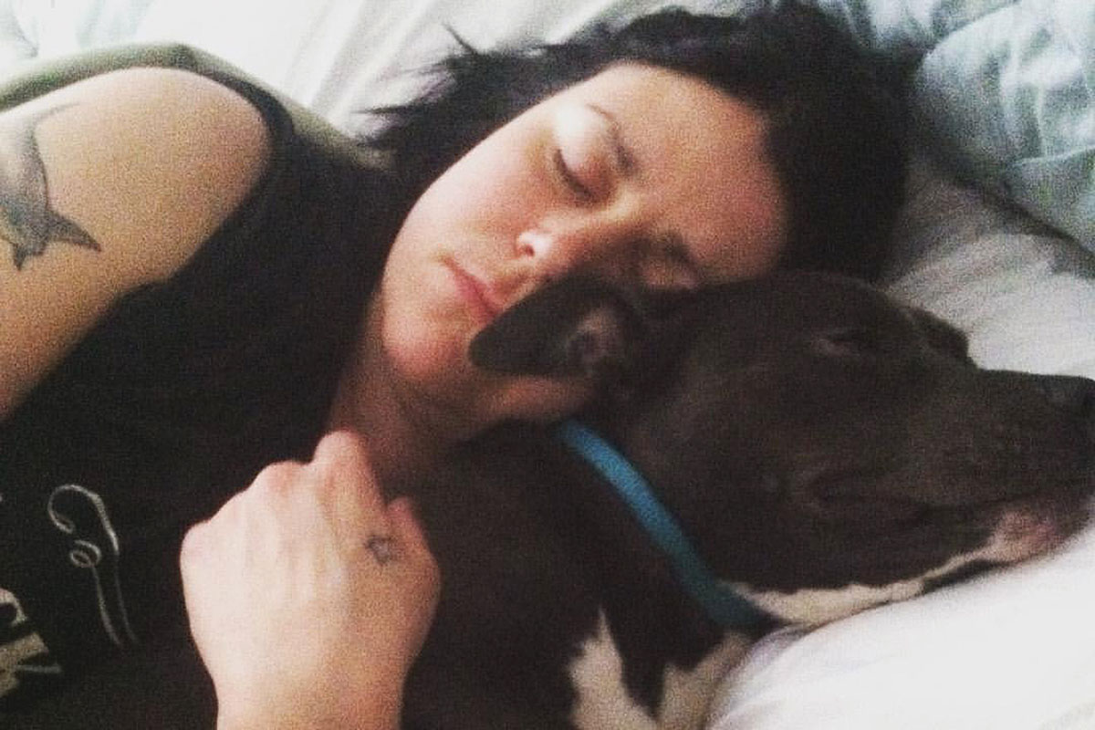 Katie Janness has her eyes closed as she lays in bed, hugging her dog, Bowie