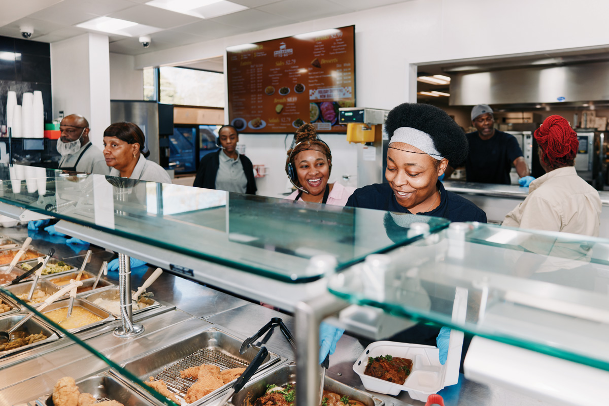 People behind the serving counter smile as the scoop food into containers
