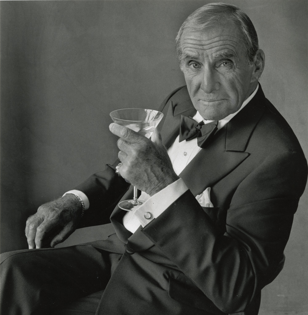 an older Big Lou sits while holding a martini glass