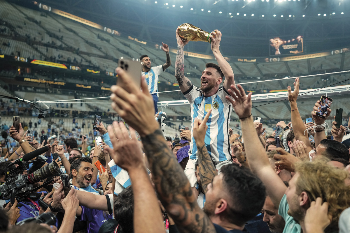 Argentina's soccer player, Messi, hold a FIFA World Cup Trophy amongst a cheering crowd
